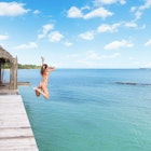 A woman jumps off a wooden platform into the blue waters in Bastimentos, Bocas Del Toro Panama.
